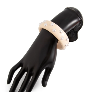 Primer plano de brazalete ancho de resina crema con doble fila de perlas en mano negra