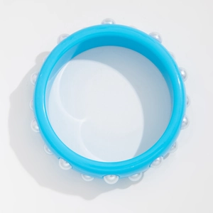 Primer plano de un brazalete de resina azul claro con perlas blancas sobre fondo blanco