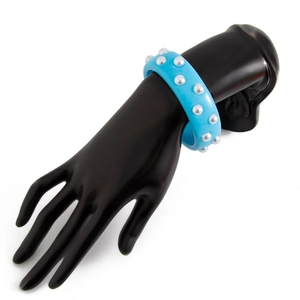 Detalle macro de pulsera ancha de resina azul cielo con perlas plateadas en modelo de mano