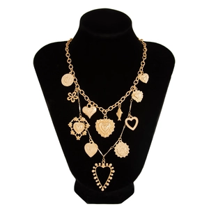 Detail of layered gold necklace featuring textured heart and sun face charms on a black bust