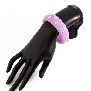 Primer plano de un brazalete ancho de acrílico lavanda con dos filas de perlas blancas