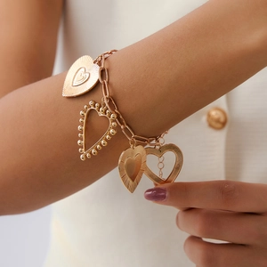 Detail view of a gold chain bracelet with four distinct heart-shaped charms on a model