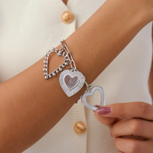Close-up of silver heart pendants on a textured curb chain bracelet worn by a model