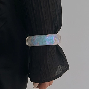 Primer plano de brazalete ancho de resina iridiscente con brillo perlado en manga