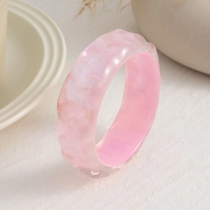 Detalle de brazalete ancho de resina rosa translúcida con textura perlada sobre piedra