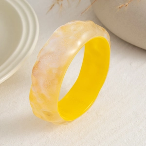 Primer plano de un brazalete de resina amarilla con texturas artísticas y diseño moderno