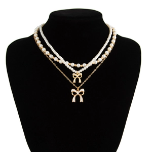 Double-layered gold chain and pearl necklace featuring two white enamel bow pendants