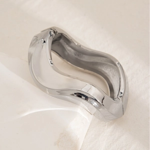 Close-up of polished silver wavy bangle with irregular texture on marble surface