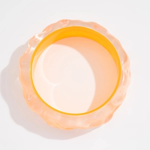 Detalle de brazalete ancho de resina ondulada en tonos naranja y rosa suave