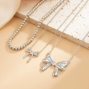 Close-up of silver bow pendant necklaces with pearls on aesthetic stone props