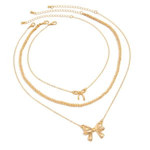 Detailed view of triple-layered gold necklaces with pearl beads and bow pendants