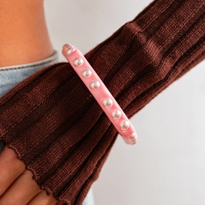 Brazalete de resina rosa con perlas sintéticas sobre una manga de punto oscuro