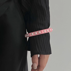 Detalle de brazalete ancho de resina rosa con perlas blancas sobre una manga negra