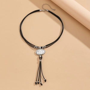 Etnische ketting met ovale metalen hanger en zwarte kwastjes op beige achtergrond