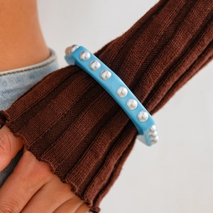 Primer plano de un brazalete ancho de resina azul con tachuelas plateadas en una manga marrón