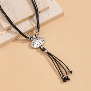 Detail of vintage ethnic oval pendant with black dotted texture and fringe on waxed cord