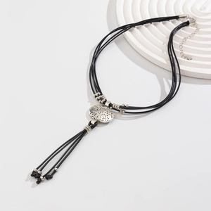 Close-up of ethnic necklace with black cord, silver disc pendant and fringe detail