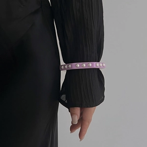 Detalle de la pulsera de resina lavanda con perlas blancas sobre manga negra