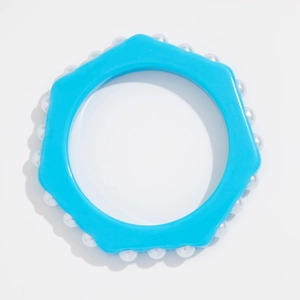 Detalle de brazalete de resina azul en forma de engranaje con perlas blancas sobre blanco
