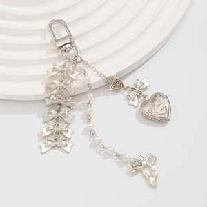 Pendentif nœud argenté avec chaîne perles et médaillon cœur sur support blanc