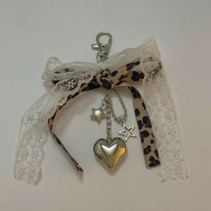 Dettaglio charm borsa fiocco in pizzo leopardato con pendenti a cuore e stella in metallo
