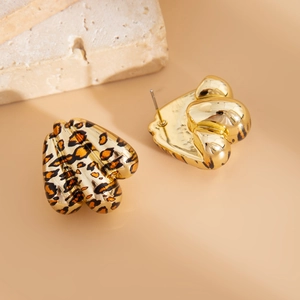 Dettaglio macro di orecchini a cuore leopardati con placcatura in oro su sfondo beige
