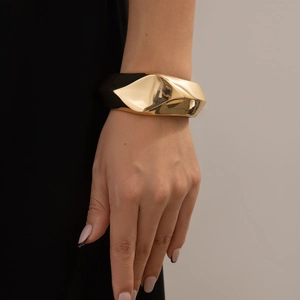 Detalle de brazalete geométrico dorado con textura plisada en la muñeca de la modelo