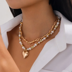 Double-layered gold necklace with pearl strand and vintage heart pendant on white shirt