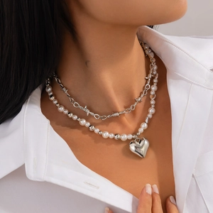 Double-layered necklace with silver thorn chain, pearls, and heart pendant on a model
