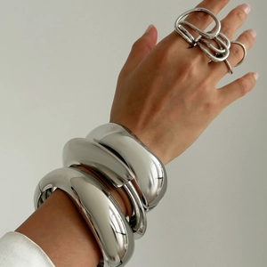 Dettaglio di spessi bracciali in argento e anello astratto sulla mano del modello