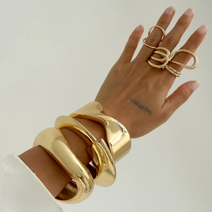 Dettaglio macro di set di bracciali rigidi dorati lucidi e anelli sulla mano della modella