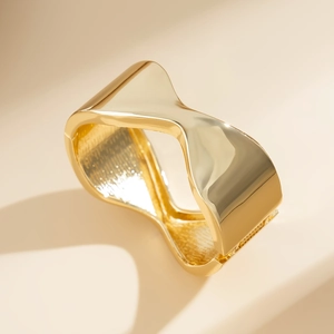 Primo piano dell'ampio bracciale dorato curvo con finitura a specchio e design moderno