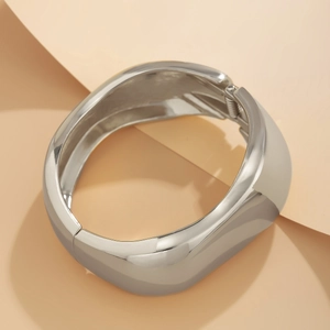 Dettaglio macro di un bracciale rigido argento lucido con curve irregolari e finitura a specchio
