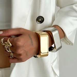 Onregelmatige metalen armbanden en gestapelde gouden ringen op model in witte blazer