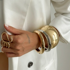 Macro shot of chunky polished metal bracelets and bold hollow ring on a silk suit