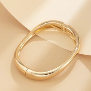 Close-up of polished gold-plated irregular oval bracelet with hinge clasp detail