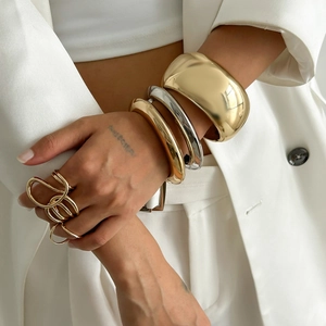Polished chunky gold cuffs and layered metal ring set worn over a white suit