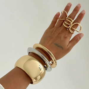 Detail of stacked chunky gold and silver bangles with irregular geometric rings on hand