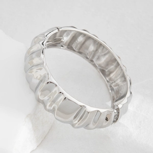 Macro detail of silver geometric wrinkled cuff bracelet on white stone surface
