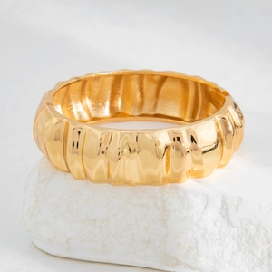 Detail of a wide gold cuff bracelet featuring 3D wavy texture on white stone base