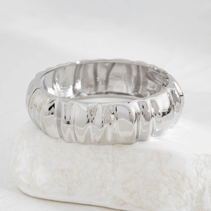 Macro view of wide silver-plated cuff with vertical pleated texture and metallic luster