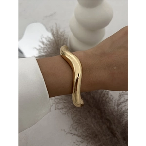 Detail of a minimalist gold irregular wave bangle with a polished metallic finish on a wrist