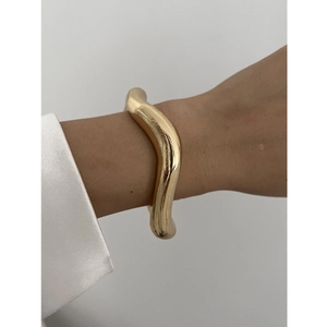 Close-up of golden irregular wave bangle with polished metal finish on a female wrist