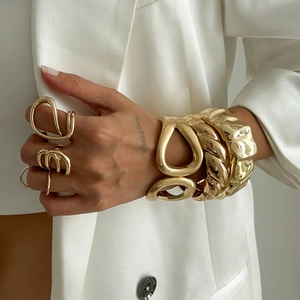 Detail of high-gloss gold hollow link and twisted rope bracelets on a white suit background