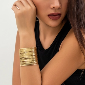 Close-up of wide gold cuff bracelet featuring multi-layer metallic wire wrap design
