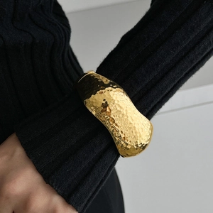 Macro shot of gold teardrop cuff bracelet with hammered texture over black sleeve