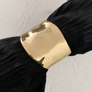 Detail of wide gold liquid metal bracelet featuring organic folds on a textured backdrop