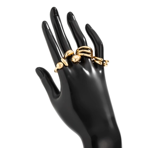 Détail d'un ensemble de bagues dorées géométriques sur un support de main noir