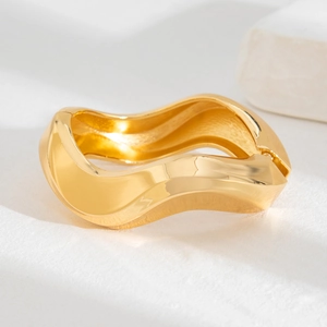 Polished gold wave-shaped open bangle with irregular curved edges on stone background