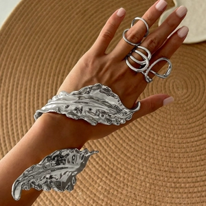 Silver liquid leaf cuff bracelet set with matching rings on a textured woven mat